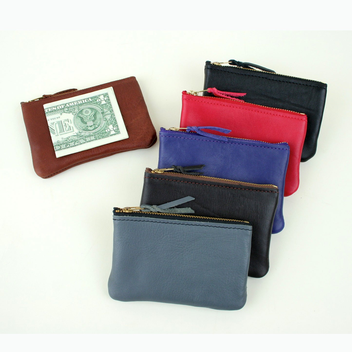 Six colors of leather coin purse with a zipper across the top, made in USA. A dollar bill folded in half is on top of one to show scale.
