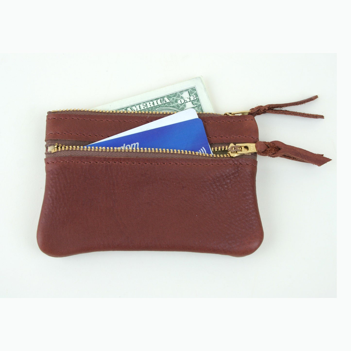 Brown leather coin purse with two zippers. A folded dollar bill and credit card are tucked in to show scale.